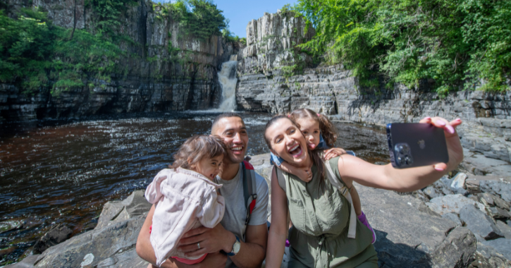Family of four taking a selfie with High Force Waterfall in the Durham Dales.